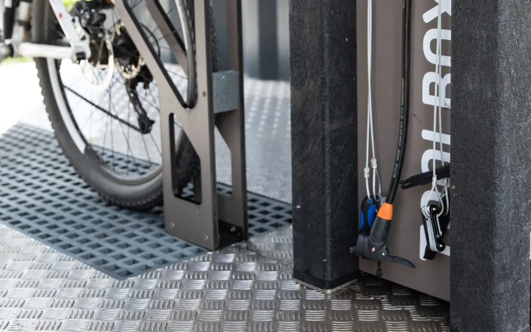 Detail of air pump and tools from the customised Floema high-tech bike station tool box, with partial view of the bike rack and waste water collection grid.