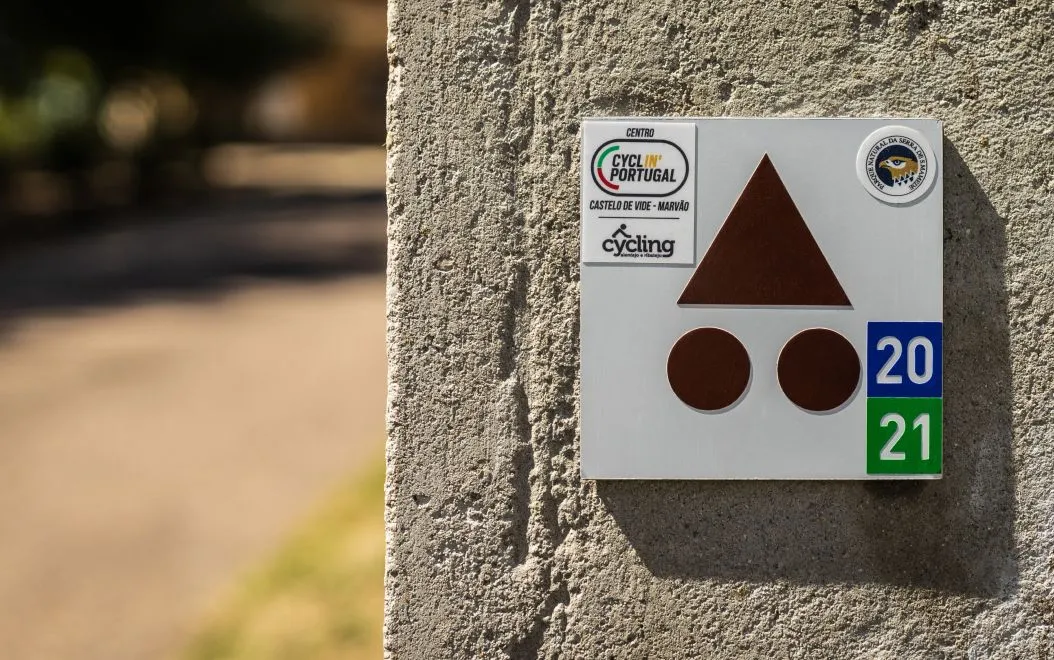 Detail of aluminium composite trail sign with route and certification stickers, installed on a wall.