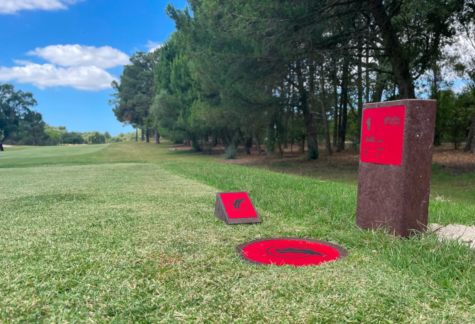 Log marker, disc marker e tee marker em área de tee de campo de golfe. Todos produzidos com estrutura em plástico reciclado castanho e com informação gravada a laser e CNC em HPL vermelho. 