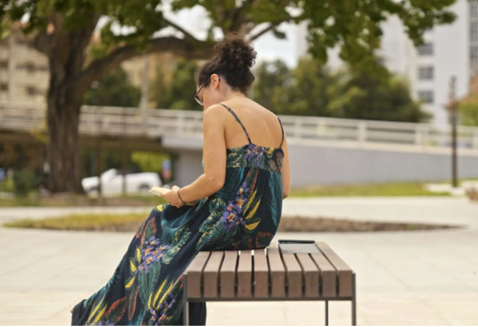 Pessoa a ler num banco inteligente feito de plástico reciclado e metal, a carregar um telemóvel no painel solar integrado.