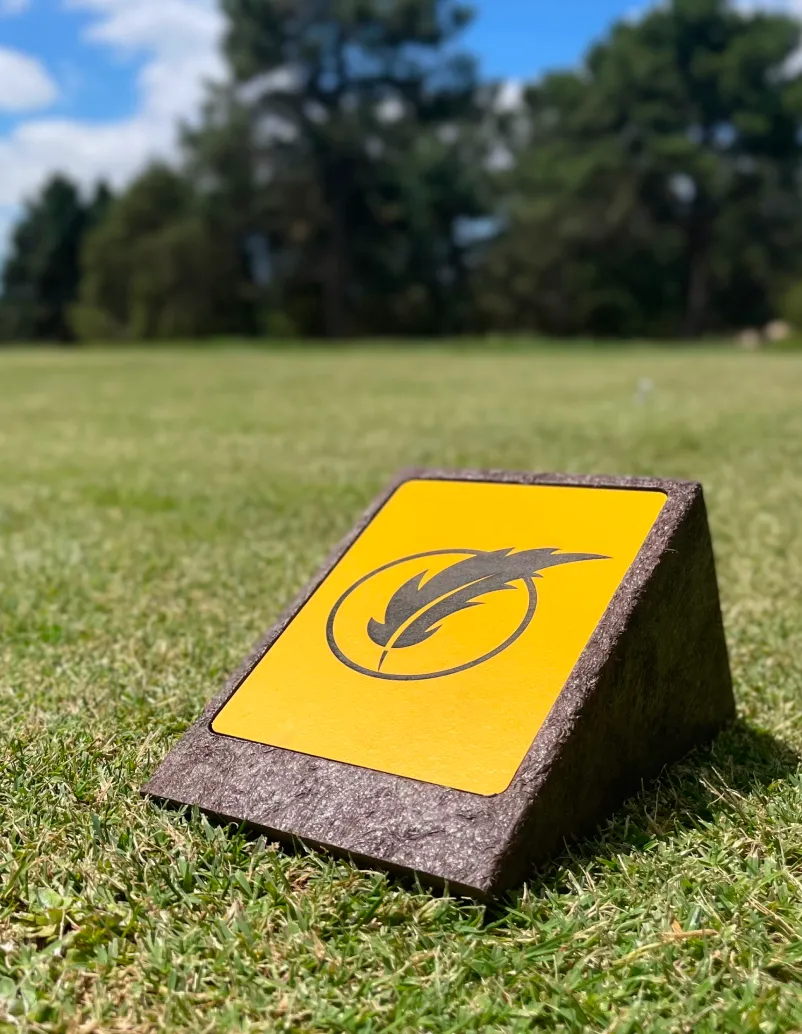 Detalhe de log marker em área de tee de campo de golfe. Com estrutura em plástico reciclado castanho e logo gravado a laser em HPL.