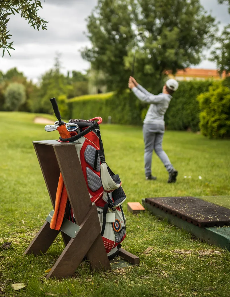 Vista lateral de bag stand Royal da Floema em plástico reciclado castanho e HPL+, com saco para tacos de golfe. Jogador de golfe em momento de swing.
