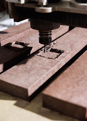 Máquina de CNC a gravar baixo relevo em perfil de plástico reciclado castanho.